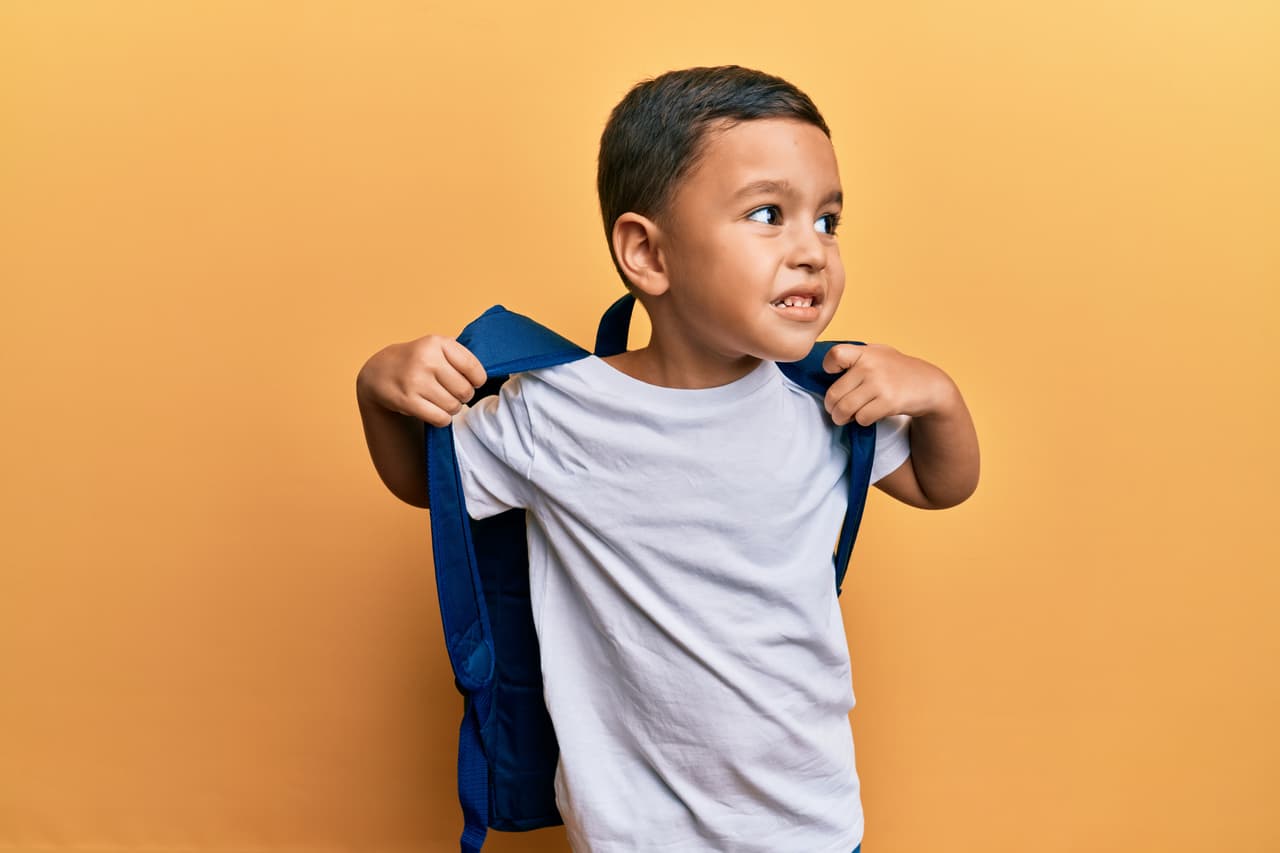 Adorable latin toddler smiling happy wearing student backpack over isolated yellow background.