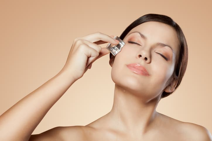 brunette woman holding ice cube on her face