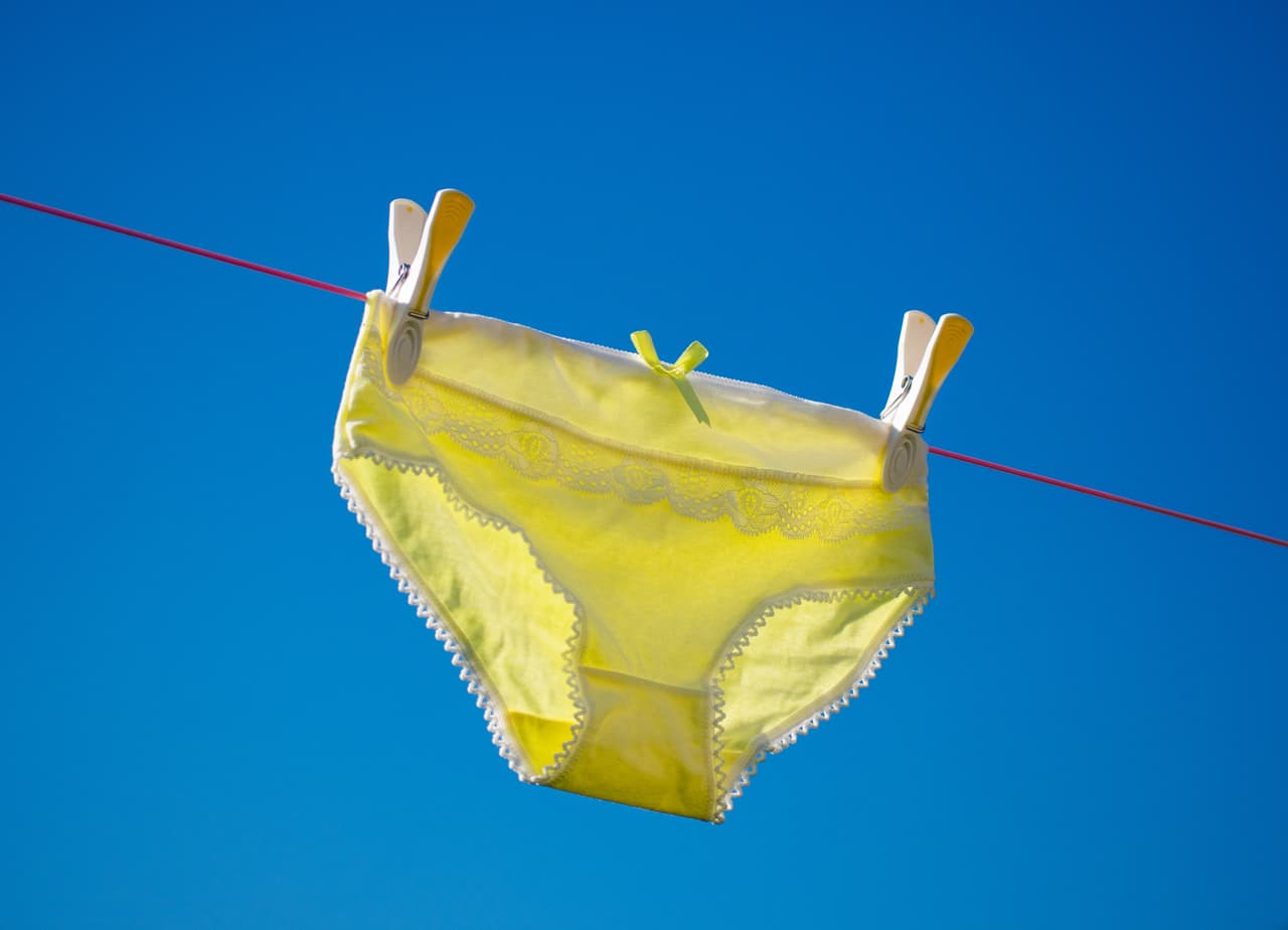 A pair of bright yellow knickers, panties, drying on the washing line, with blue sky behind.