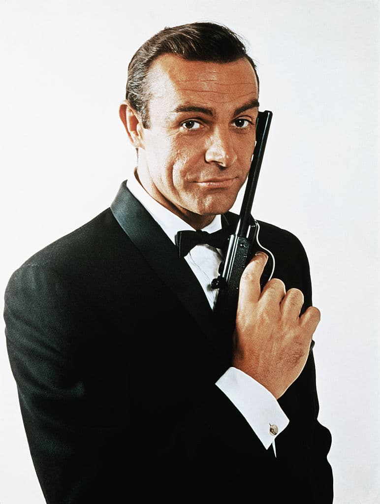 Retrato de cintura para arriba de Sean Connery, agarrando una pistola.