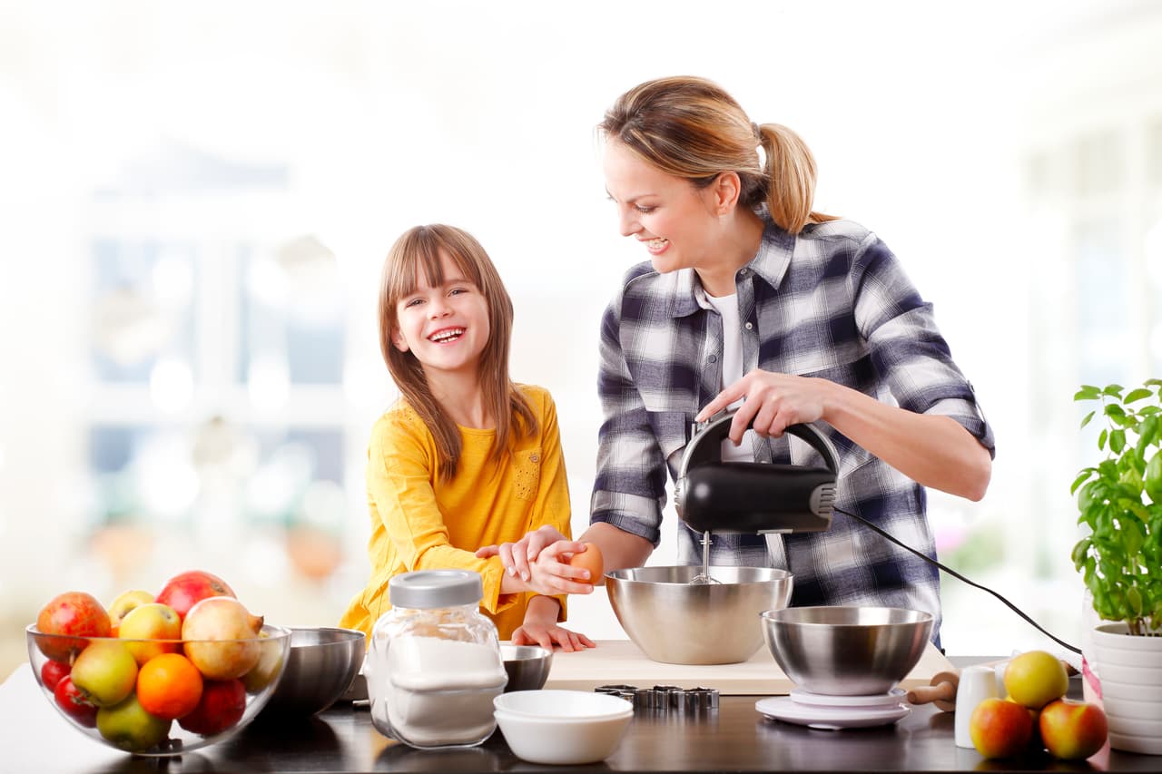 Portrait of adorable little girl and her mother baking together at home. Happy mom and her cutie daughter using kitchen robot while mixing the ingredients.
