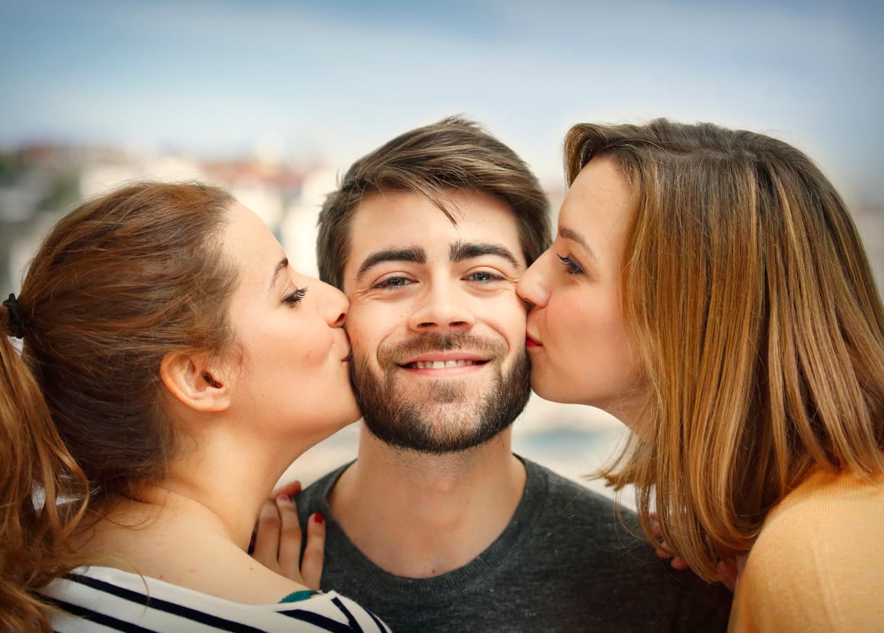 Two beautiful girls kissing a young boy