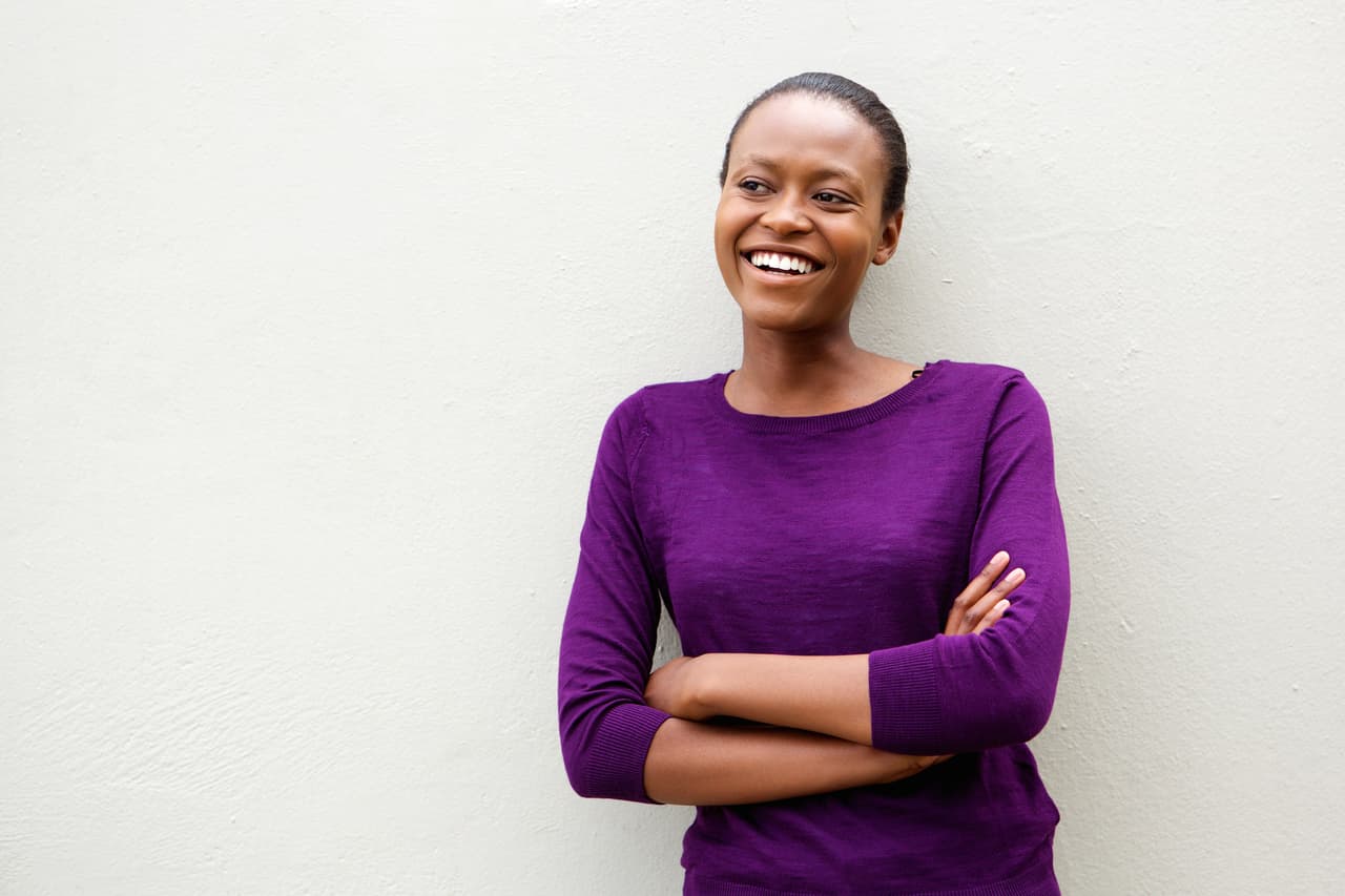 Portrait of beautiful young african woman standing with arms crossed against white wall