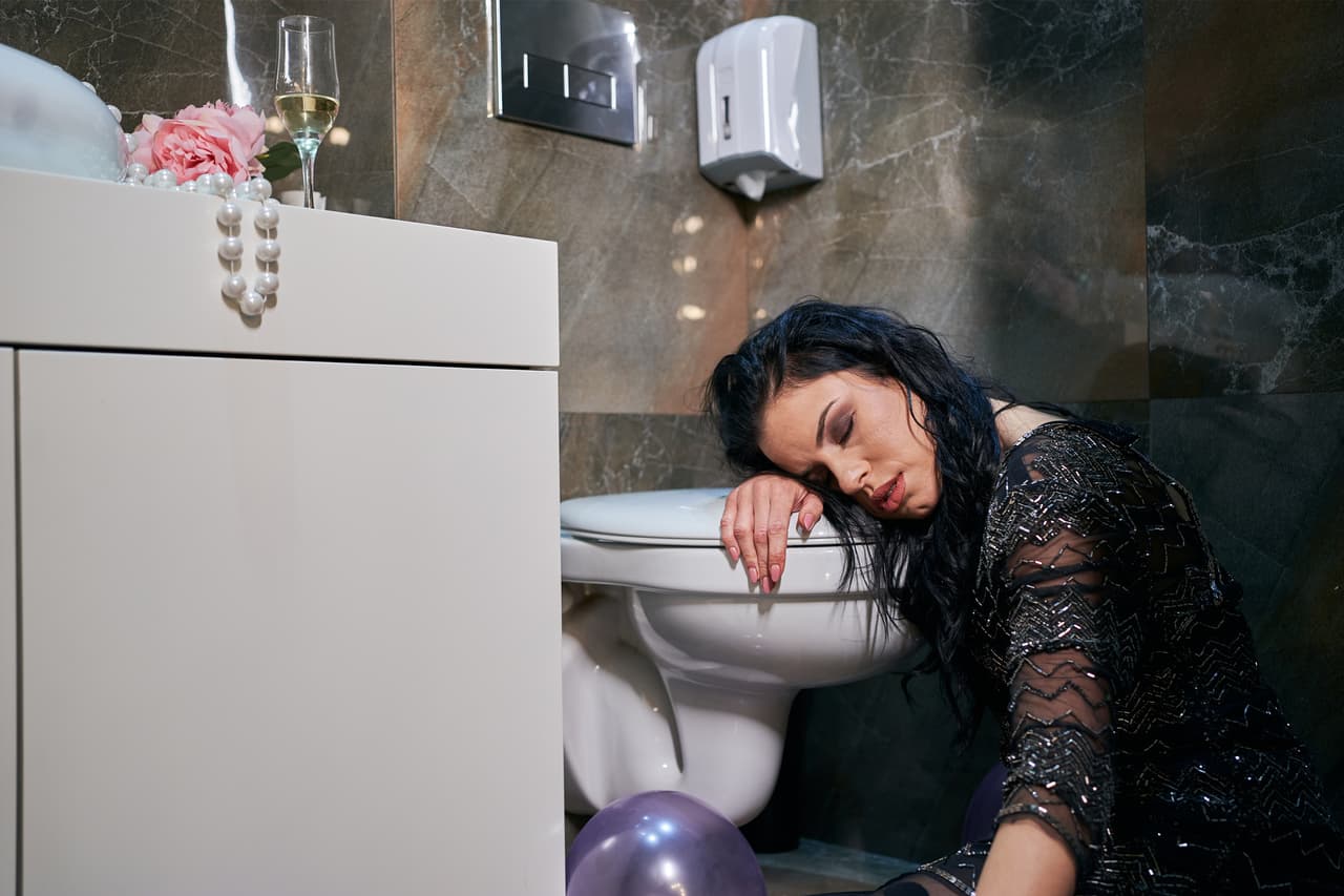 Young drunk woman sleeping on the toilet seat after she vomited