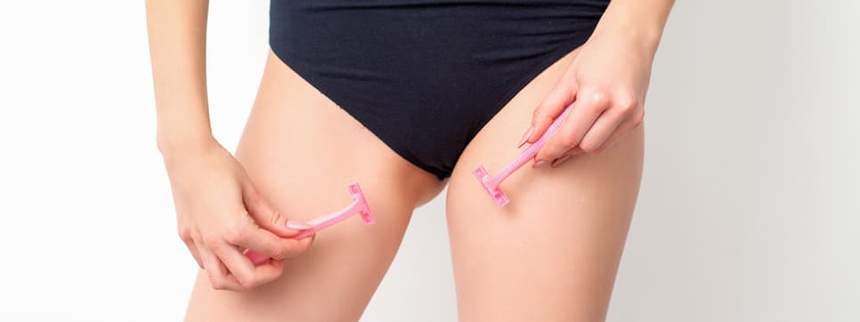 Young woman shaving crotch in bikini zone with two razors standing on white background, concept skincare and hair removal