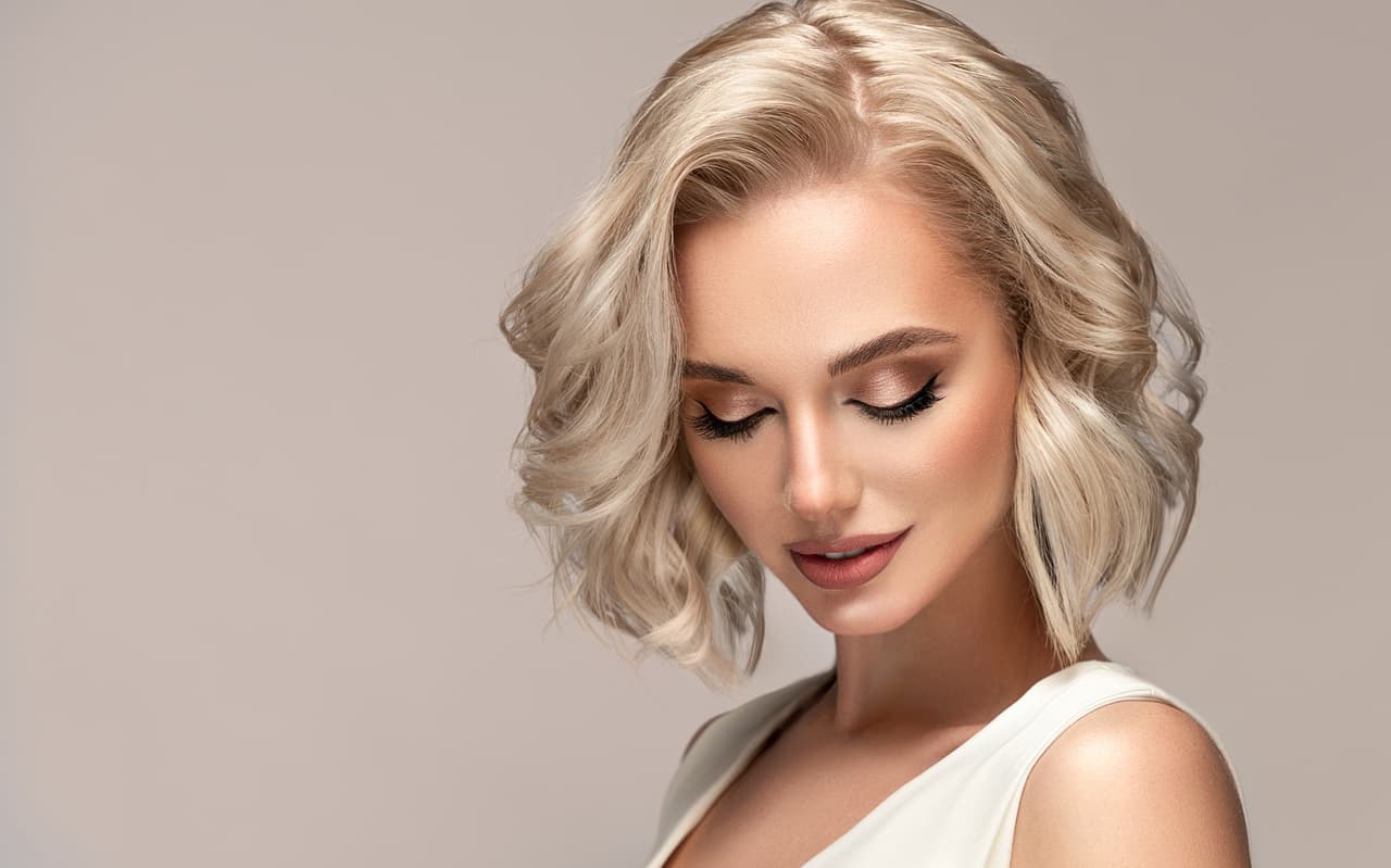 Portrait of beautiful looking young blonde woman with the middle length hair performed in elegant hairstyle. Lady wearing in a delicate makeup.Perfect model is shyly looking down. Beauty, elegance, hairstyling and cosmetics.