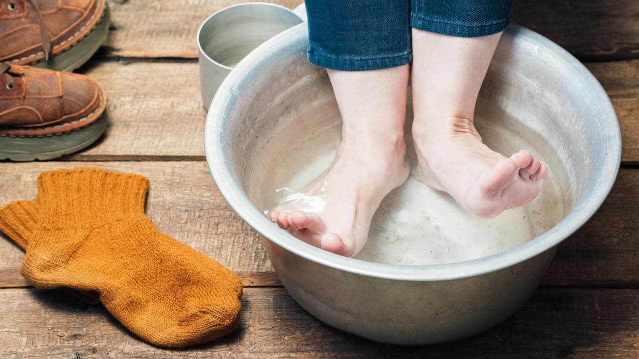 Footbath closeup. Bare feet in basin with warm water, boots and wool socks on the floor