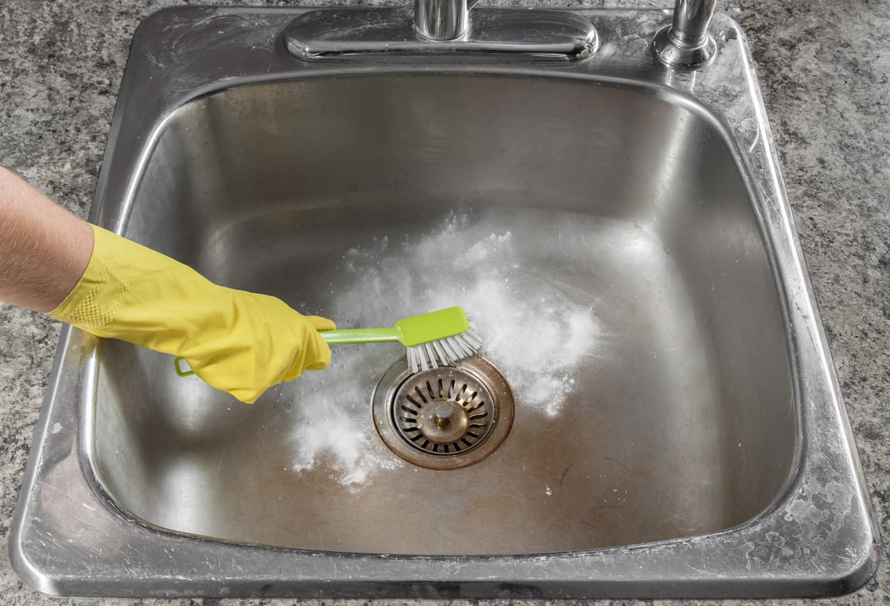 Female hand in yellow glove cleaning the kitchen sink.