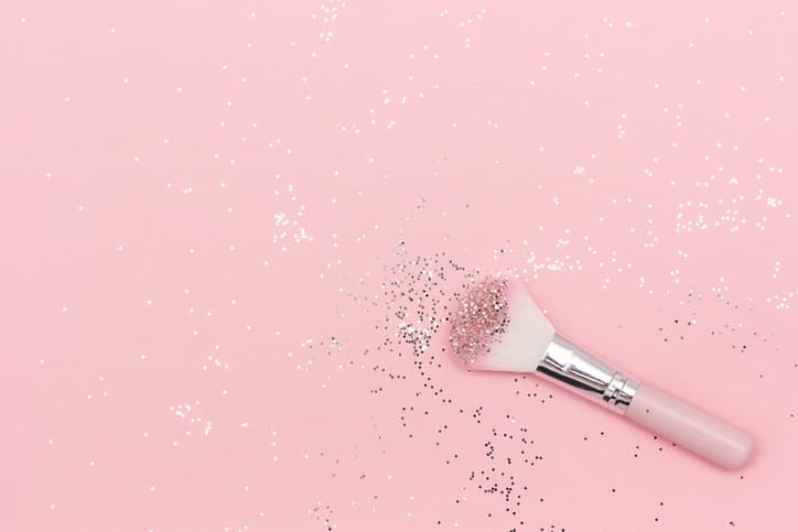 Makeup brush and shiny sparkles on pastel pink background. Festive magic makeup concept. Template for design, Top view Flat Lay Copy space.