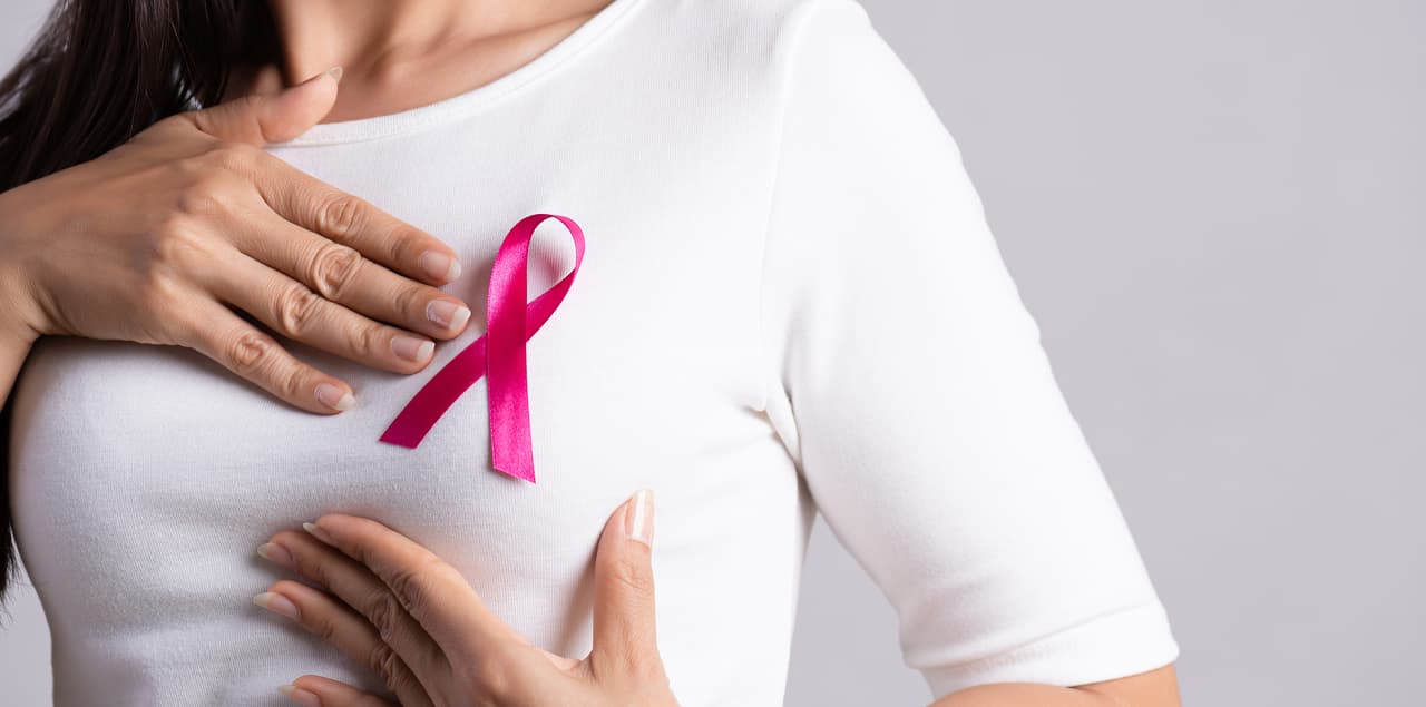 Closeup of pink badge ribbon on woman chest to support breast cancer cause. Healthcare, medicine and breast cancer awareness concept.
