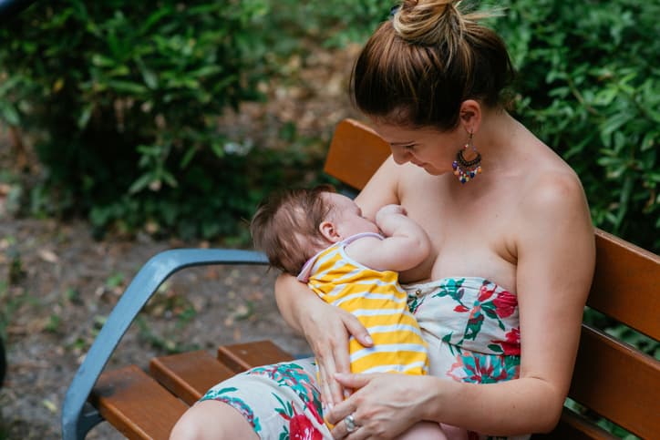 Millennial mother breastfeeding her baby girl in public. Mother and baby spending afternoon in park in summer, and mother is breastfeeding her daughter