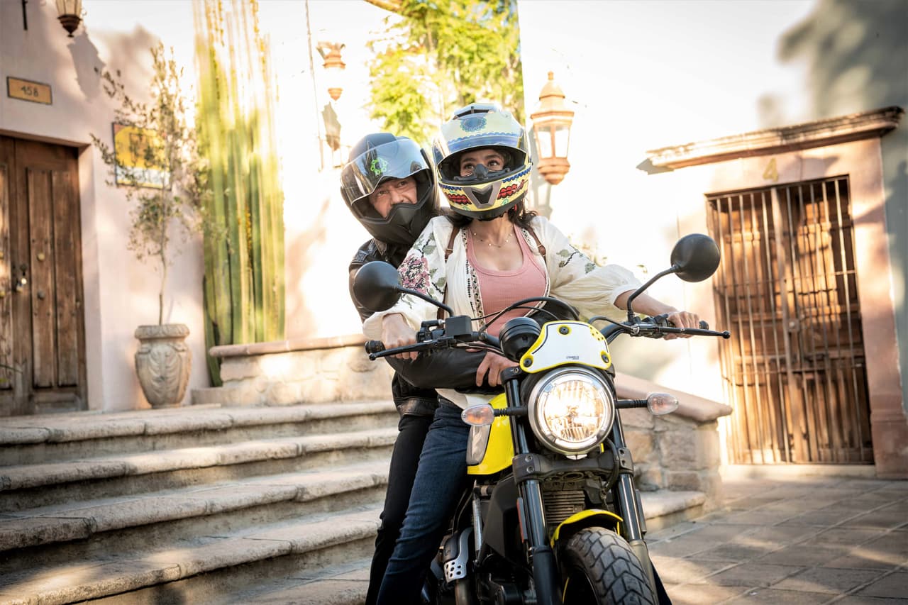 Él acepta subirse a su moto y juntos recorrer el colorido pueblo.