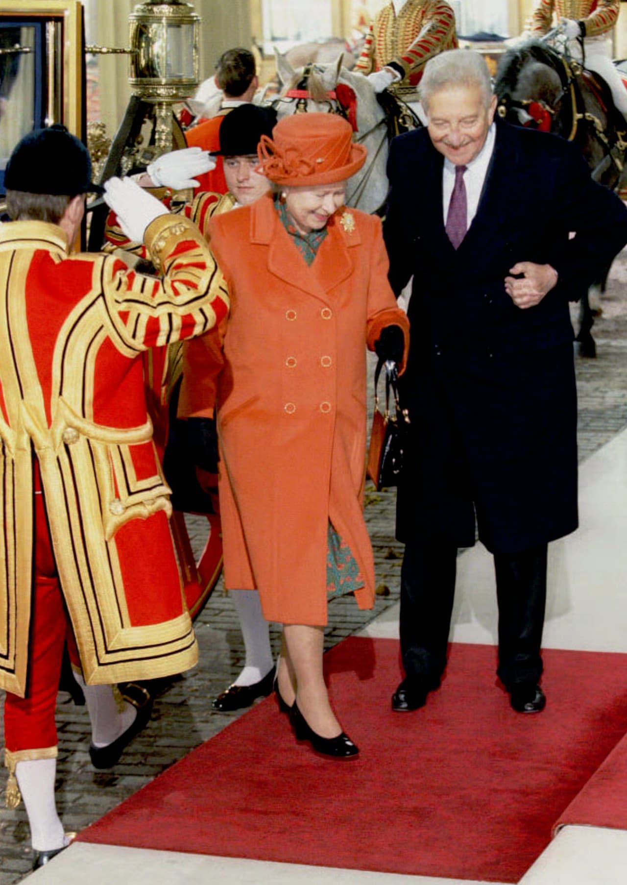 El color naranja no podía faltar en su armario, por ello la Reina Isabel II optó por un abrigo y sombrero de ese tono para su llegada al palacio de Buckingham en 1997.