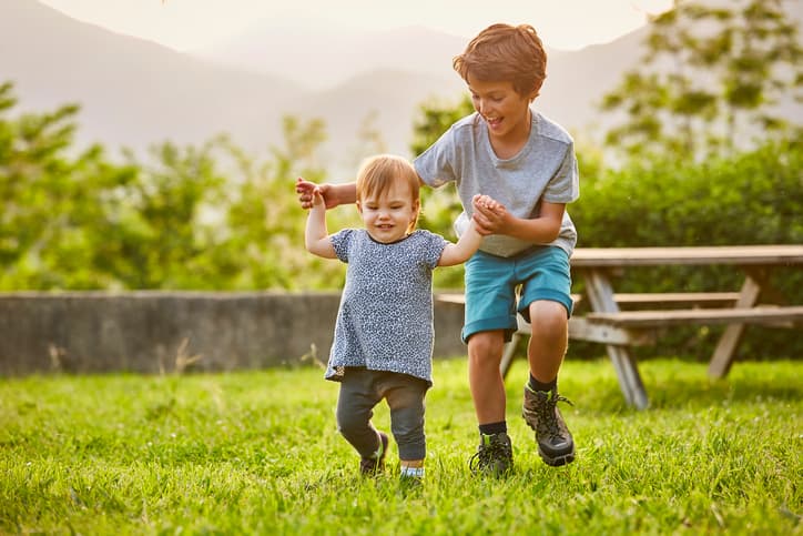 Happy boy playing with toddler on grassy field. Kids are wearing casuals. They are enjoying at back yard.