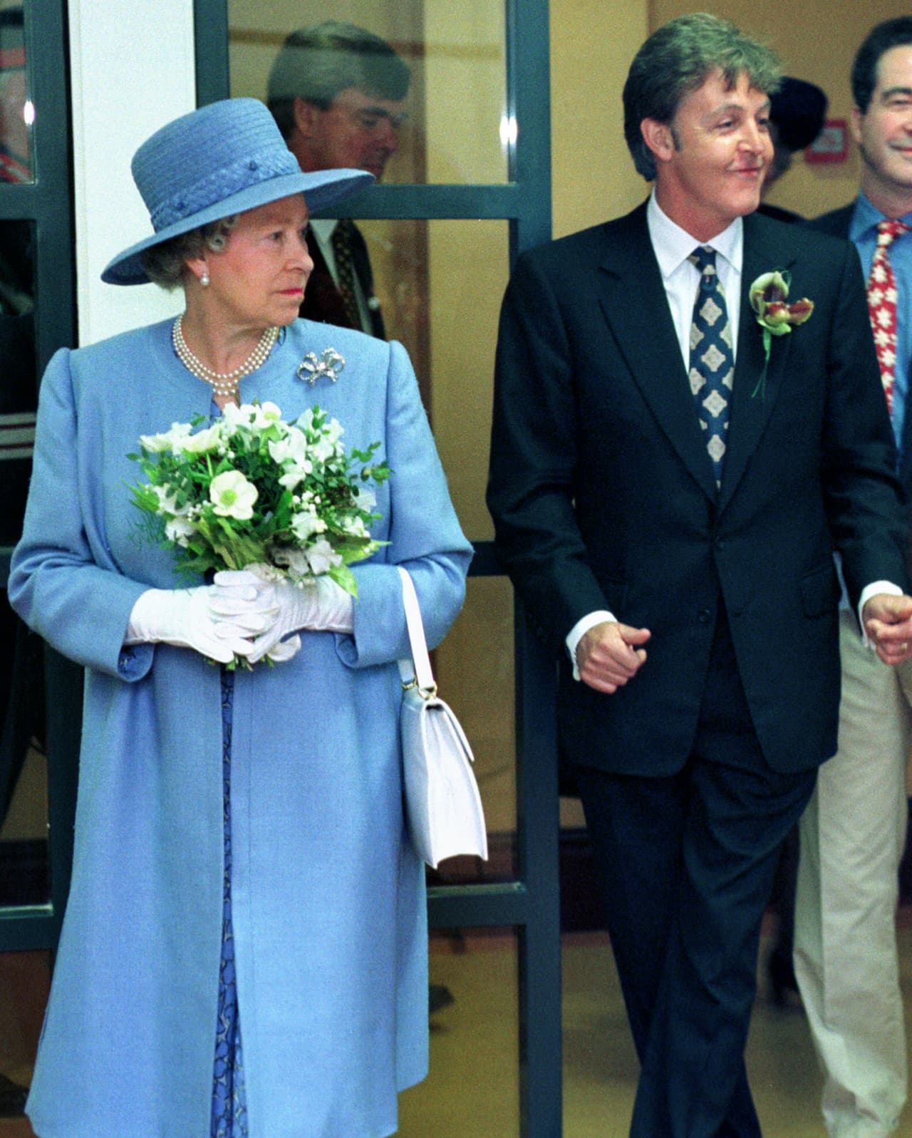Isabel II, quien optó por un abrigo azul cielo, al igual que su sombrero, y Paul McCartney apreciaron la actuación de un grupo de estudiantes en el Instituto de Artes Escénicas de Liverpool en junio de 1996.