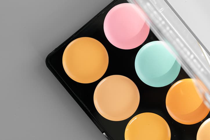 Make-up palette with colorful concealers on gray background close up