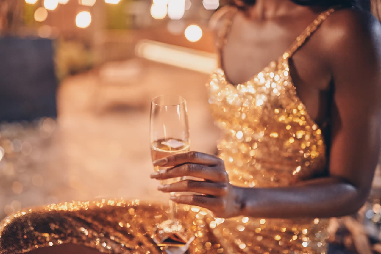 Close-up of beautiful young African woman in evening gown holding flute with champagne while spending time on night party