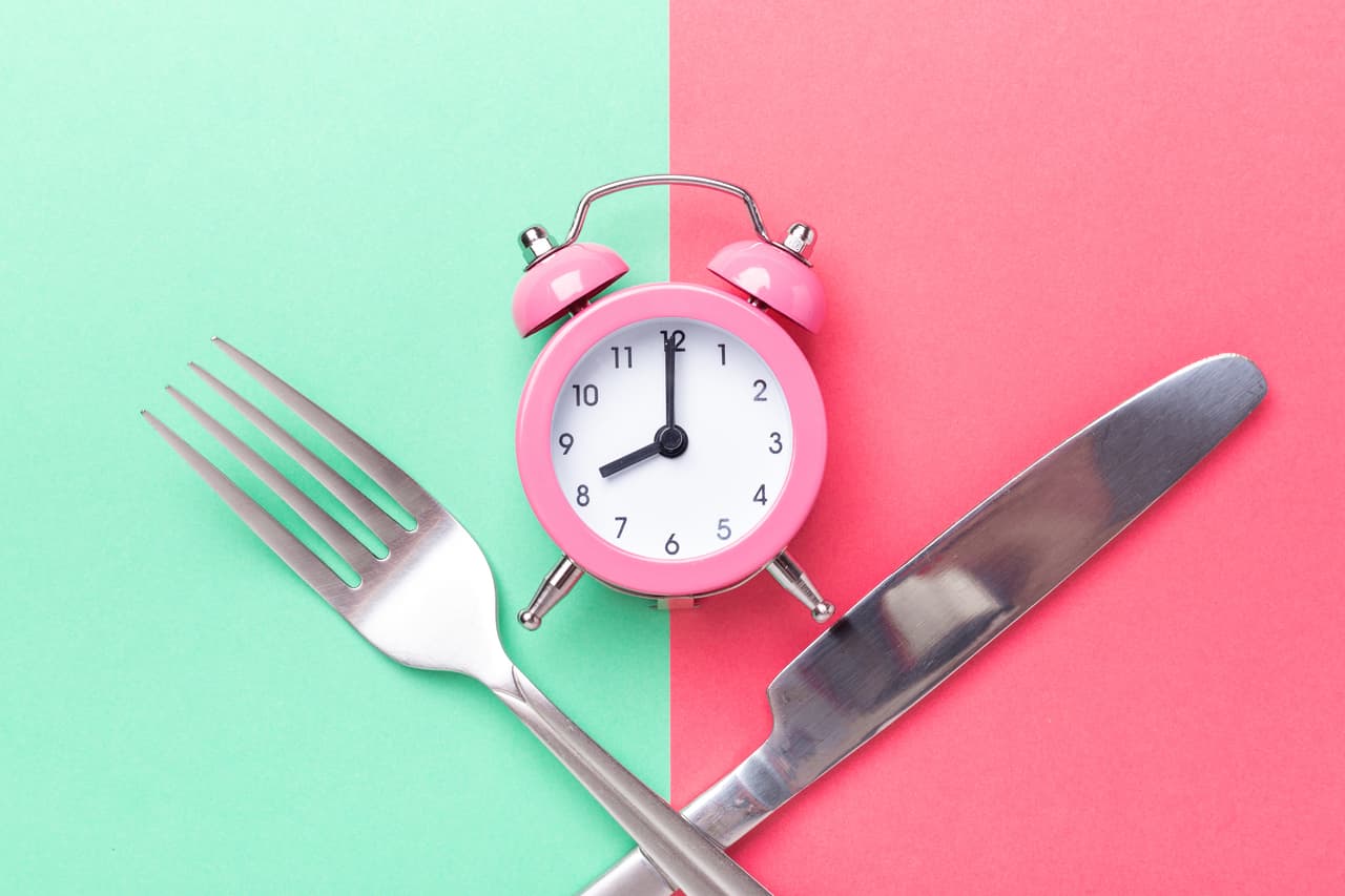 Pink alarm clock, fork, knife on colored paper background. Intermittent fasting concept - Image