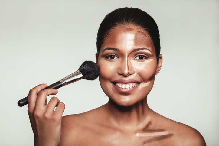 Close up portrait of contour and highlight makeup on female model. Woman applying makeup on her face with brush.