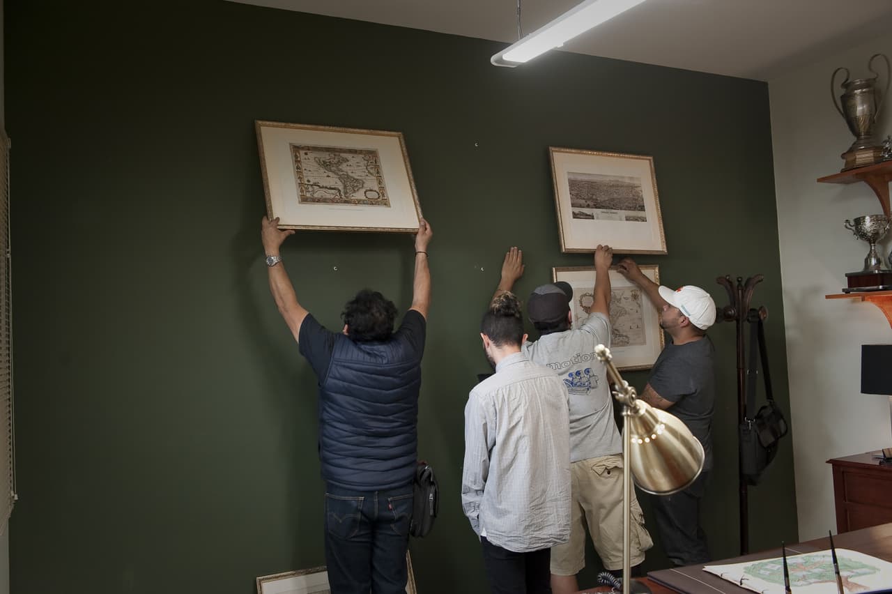 El equipo de producción prepara la oficina del director y ensaya el movimiento de los cuadros, que Carlitos se encargará de mover con sus poderes.