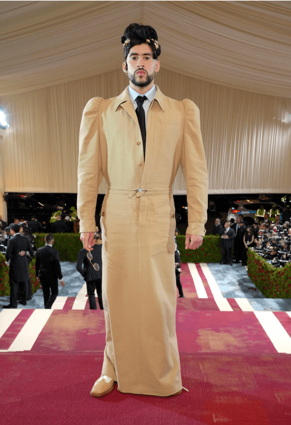 Bad Bunny - el boricua del momento también asistió a la gala listo para romper estereotipos con un look de Burberry que constó de un vestido beige que combinó con una camisa blanca con corbata negra, y un peinado de chongo alto y voluminoso.